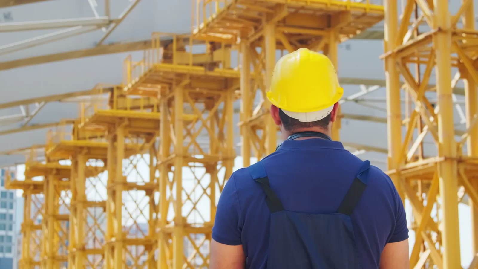 A site worker in a hard hat looking up at a crane
